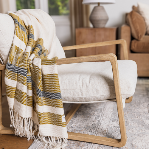 Modern lounge with the Luxe Bamboo Stripe Throw in Natural & Brass, draped over clean-lined seating—soft texture meets golden warmth